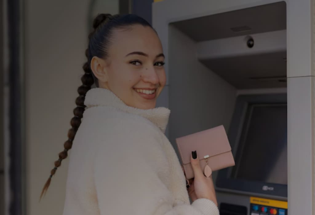 Клиент банка Уралсиб у терминала самообслуживания партнерской сети, улыбается после успешного получения средств без комиссии