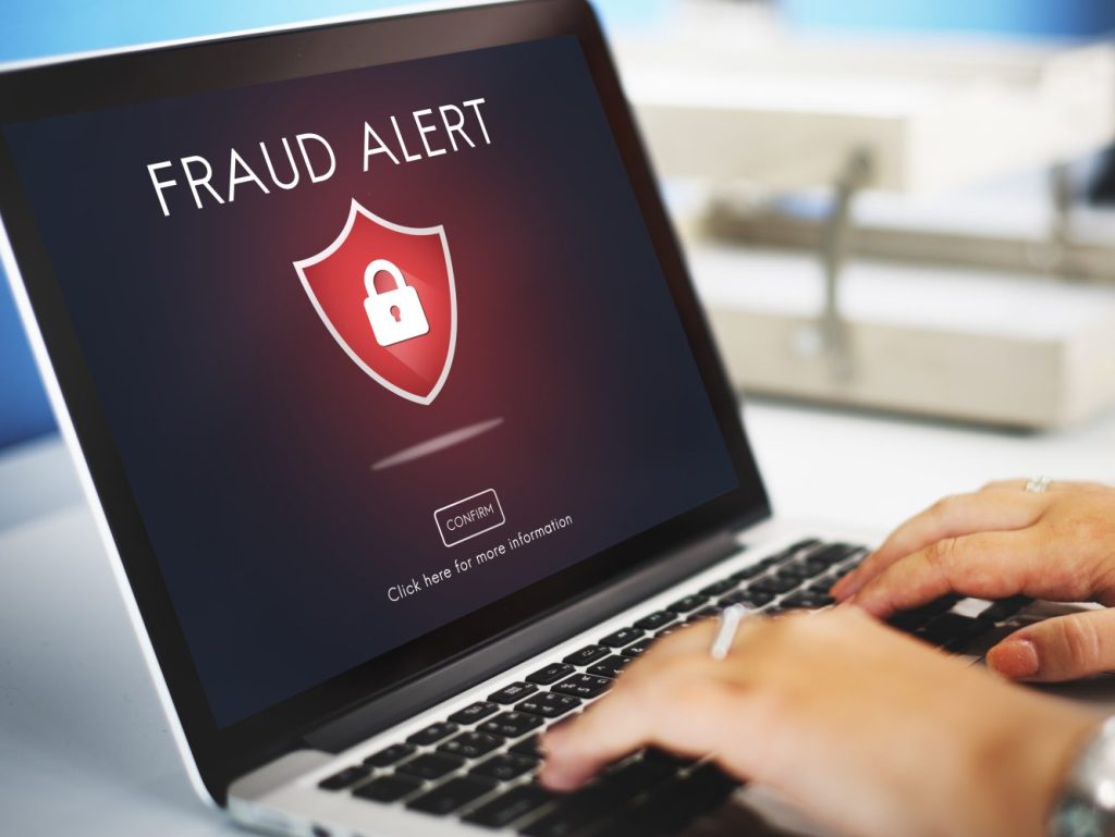 Ноутбук с надписью Fraud Alert и красным щитом — заём, оформленный мошенниками на чужие данные